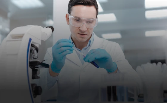 A scientist working in a lab, next to a microscope.